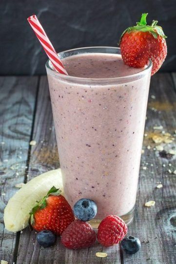 a smoothie in a glass with strawberries and blueberries on the rim next to it