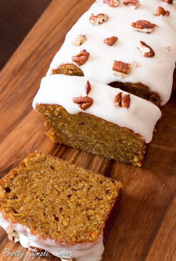 a loaf of carrot bread with white frosting and pecans on top, sitting on a wooden cutting board