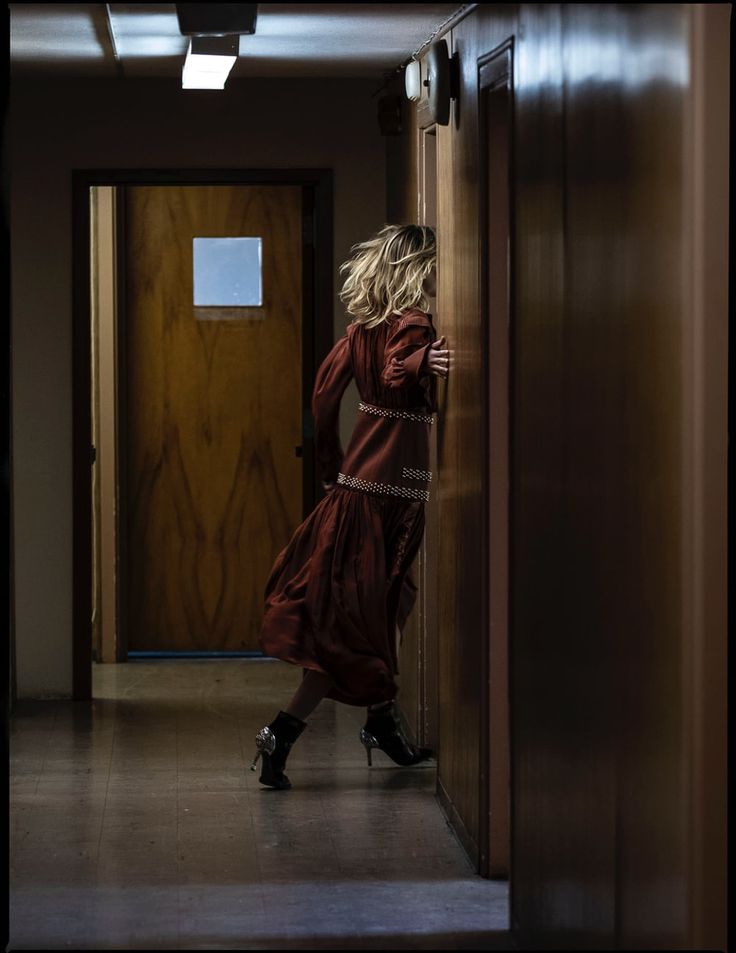 a woman in a long red dress is standing by a door and looking at something