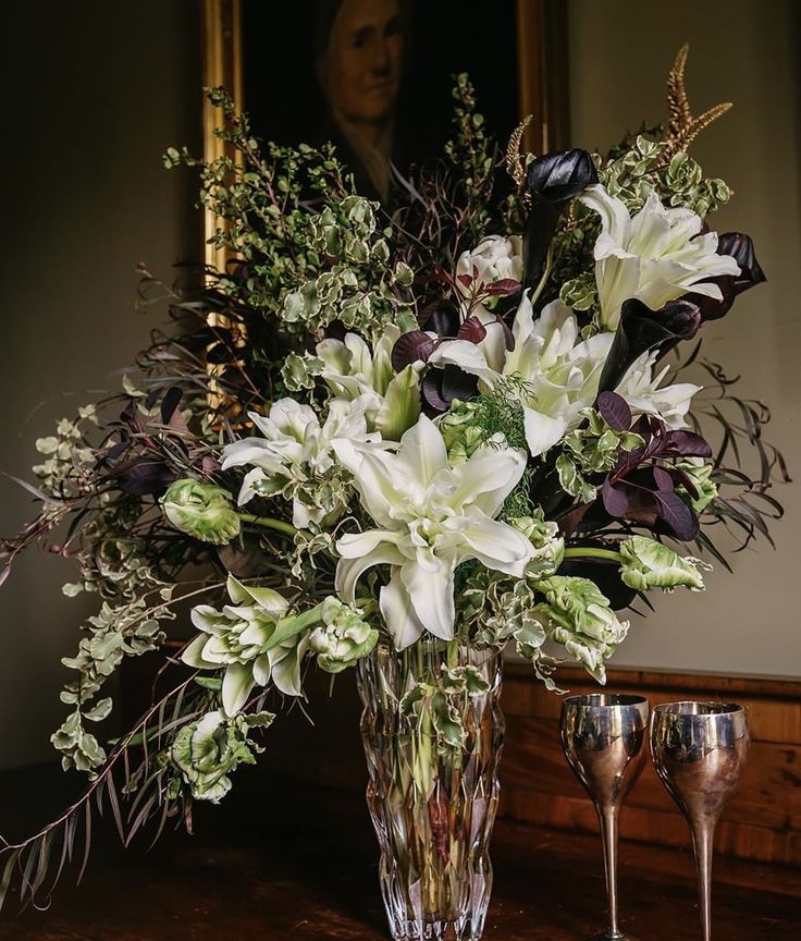 a vase filled with white flowers on top of a wooden table next to two wine glasses