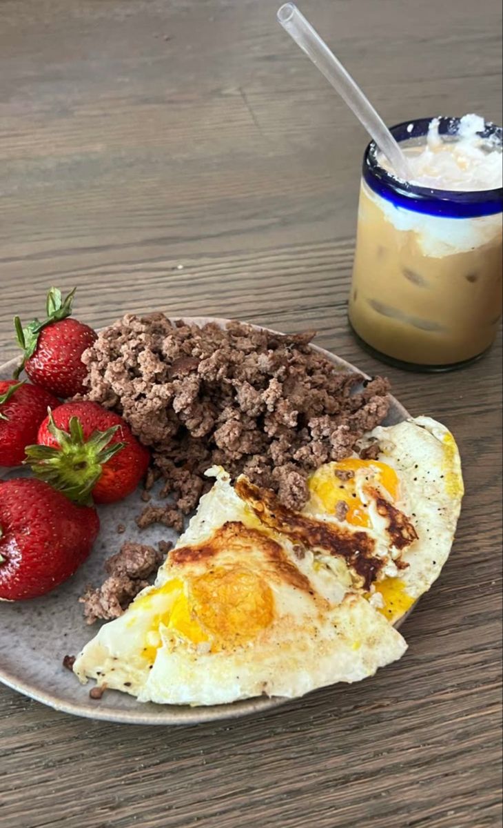 a plate with eggs, meat and strawberries on it