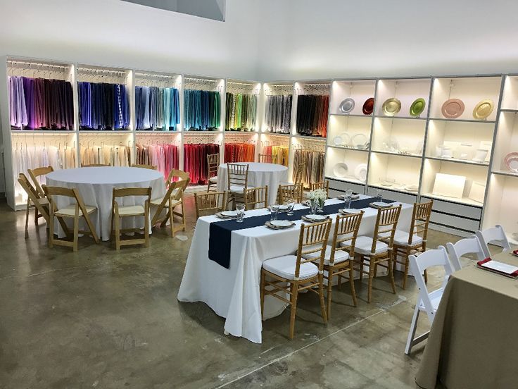 a room filled with lots of tables and chairs covered in white tablecloths next to shelves