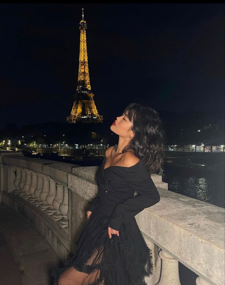 a woman in black dress standing next to the eiffel tower