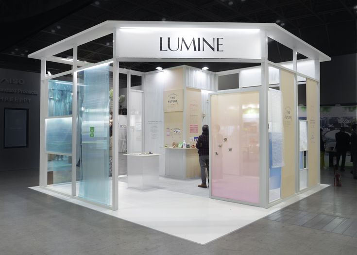 a woman standing in front of a white and pink display booth at a trade show