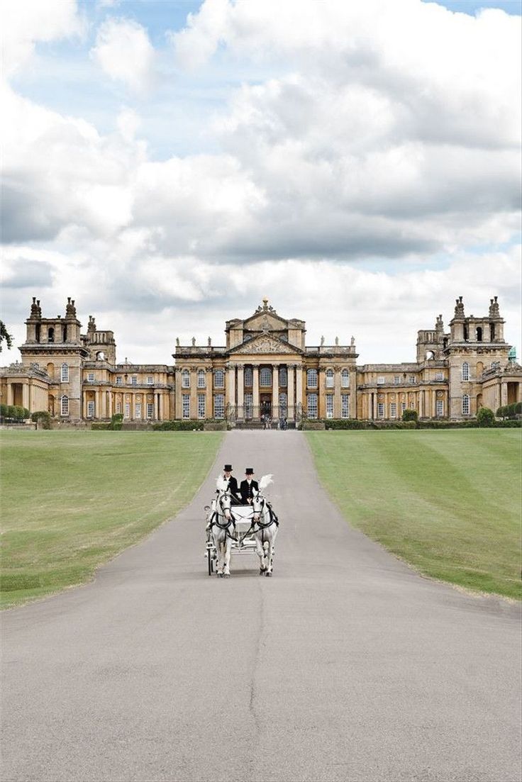 two people riding in a horse drawn carriage down a road next to a large building