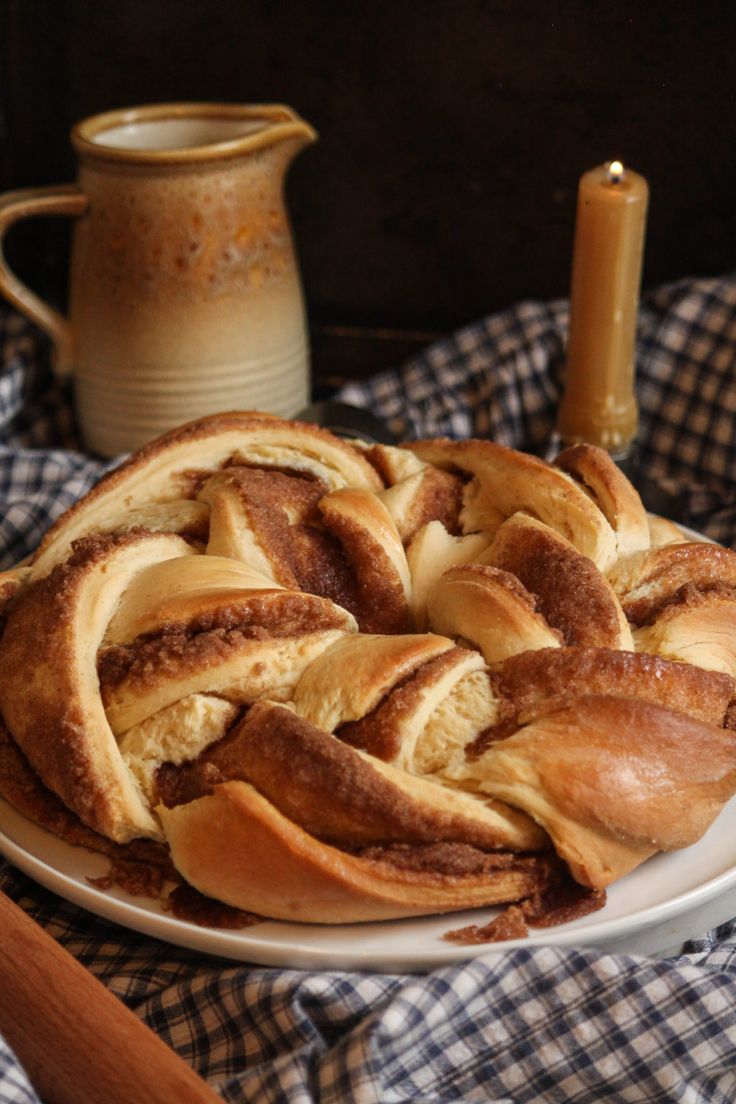 a white plate topped with pastry next to a cup and candle on a checkered table cloth