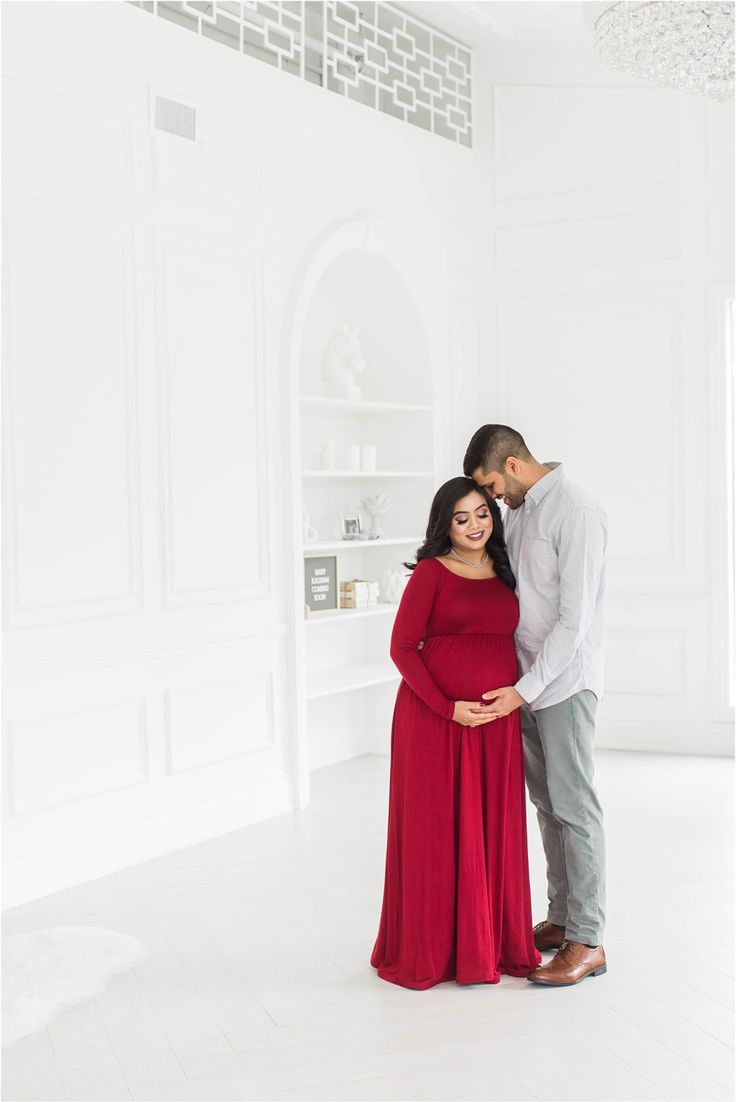 a pregnant woman in a red dress standing next to her husband