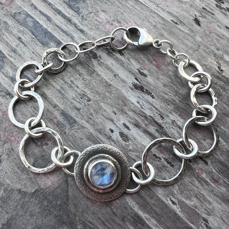 This handmade bracelet is created from solid sterling silver and Rainbow Moonstone. I have set a glowing Rainbow Moonstone cabochon in sterling and fine silver. The natural stone is framed by a series of sterling silver links which I have formed, soldered, and hammered by hand. The bracelet features a 1-inch extender chain allowing it to be worn from 6.75-7.75 inches in total length. The silver has been oxidized and polished to create an antique patina finish.Be sure to see all photos and video Sterling Silver Bracelet With Gemstone And Moonstone, Silver Artisan Bracelet With Cabochon, Artisan Silver Bracelet With Cabochon, Silver Spiritual Bracelets With Moon Phase, Artisan Sterling Silver Round Bracelet, Silver Bracelets With Natural Moonstone, Unique Sterling Silver Bracelet With Natural Stones, Silver Moonstone Bracelet With Natural Stones, Silver Moonstone Fusion Jewelry