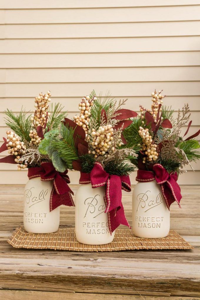 three white mason jars with red bows and greenery are sitting on a wooden table