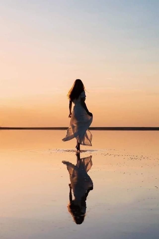 a woman is walking across the water at sunset