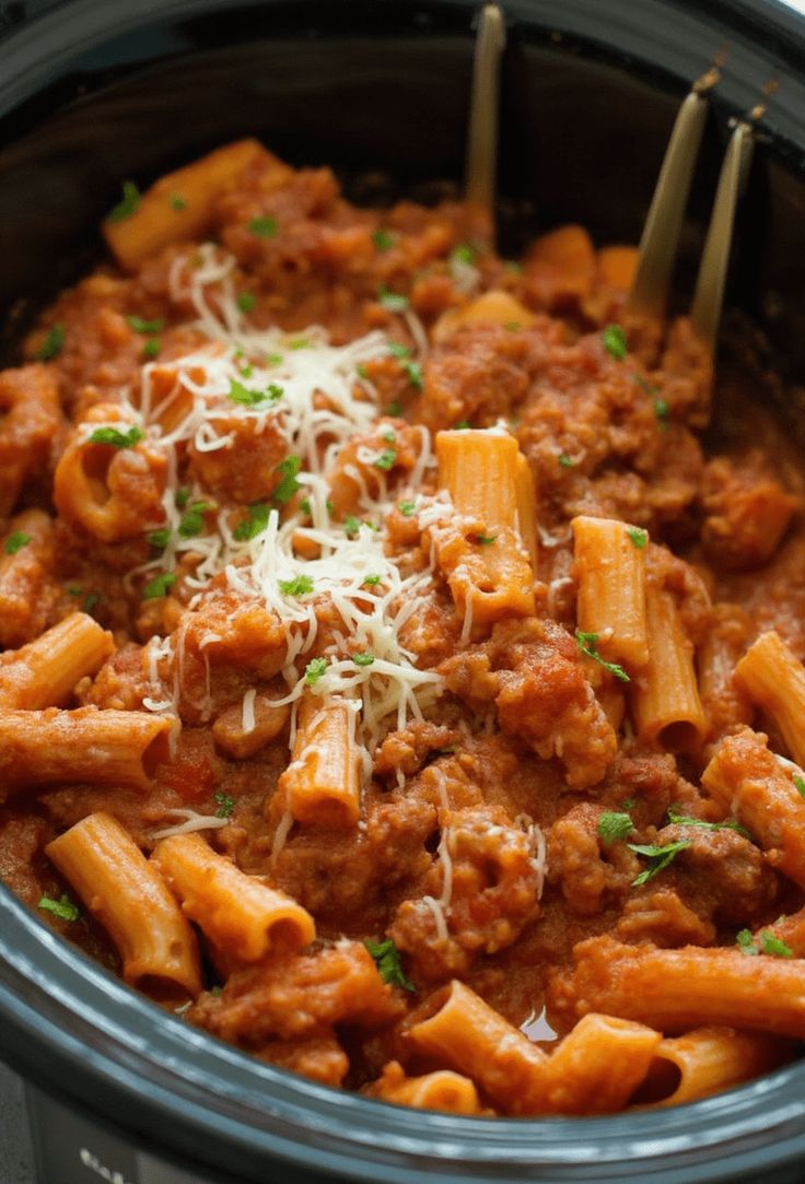 a crock pot filled with pasta and meat sauce, garnished with parmesan cheese