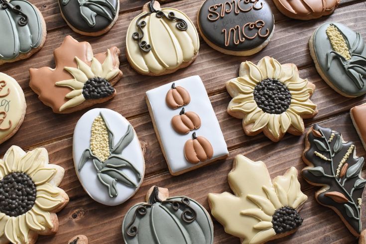 many decorated cookies on a wooden table with pumpkins and sunflowers in the center