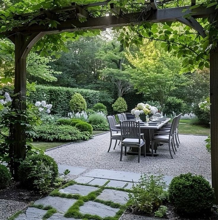 an outdoor dining table and chairs under a pergolated trellis in the middle of a garden