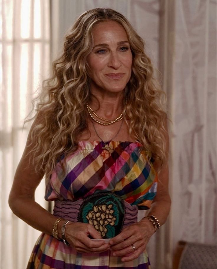 a woman in a multicolored dress is holding a small purse and looking at the camera