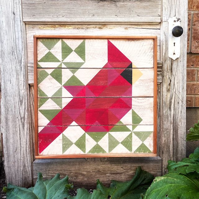 a red bird painted on wooden planks in front of some green leaves and plants