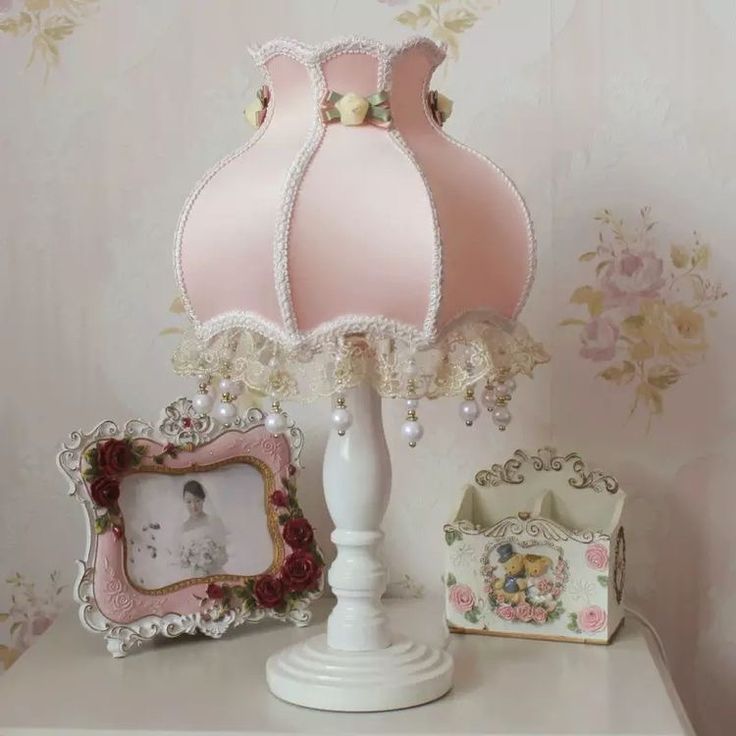 a pink lamp sitting on top of a white table next to two pictures and a frame