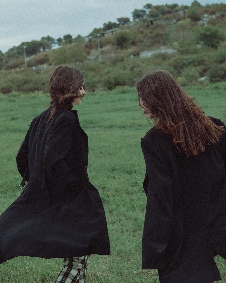 two women in black coats are walking through the grass