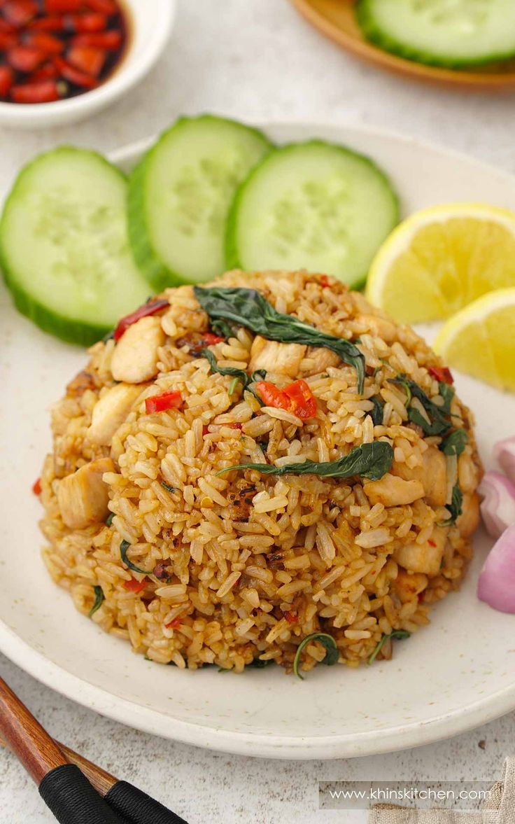 a white plate topped with rice next to sliced cucumbers and lemon wedges