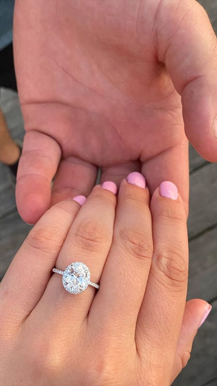 a woman's hand holding an engagement ring on top of another person's finger