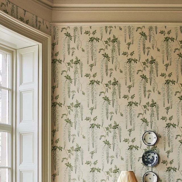 a lamp on a table in front of a wallpapered room with two vases