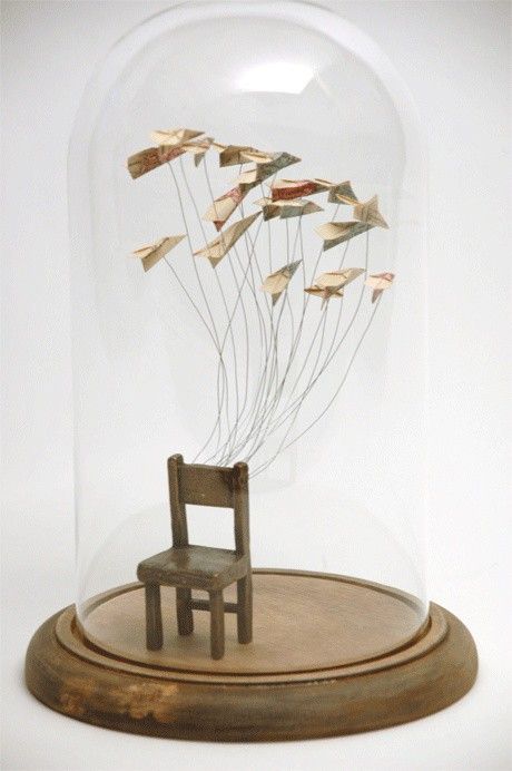 a wooden chair under a glass dome with paper birds flying in the air above it