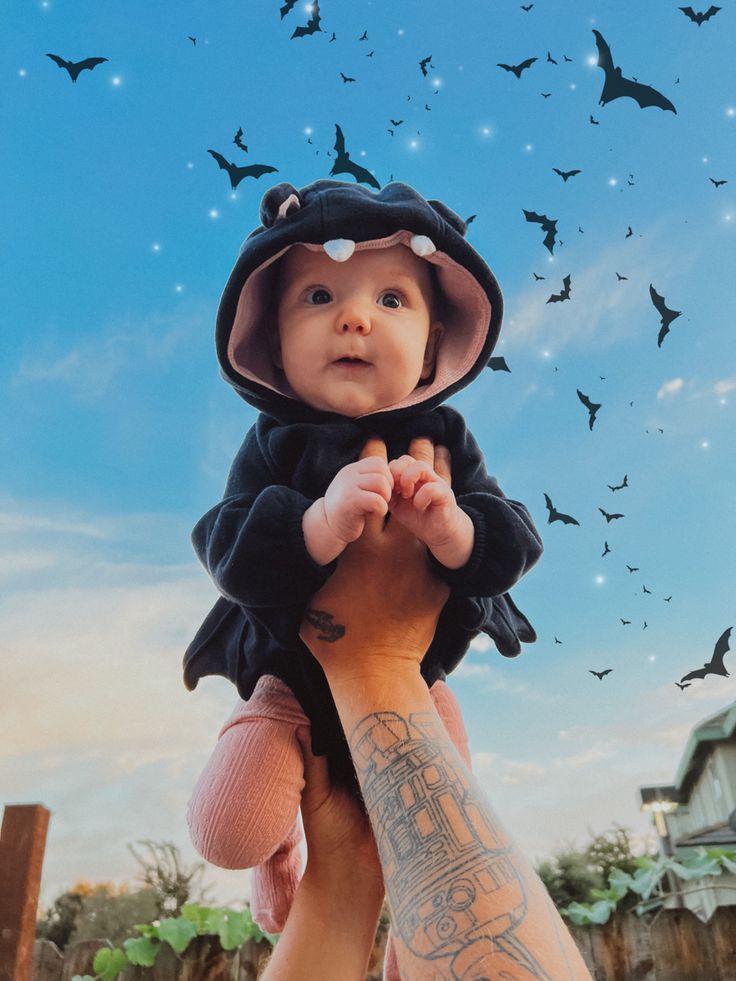 a person holding a baby in their arms with bats flying above the sky behind them