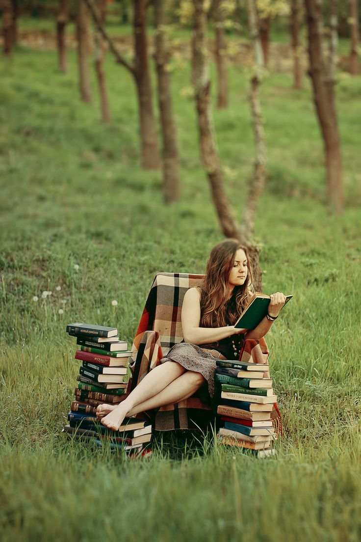 a woman is sitting on a chair with books in her lap and reading the book