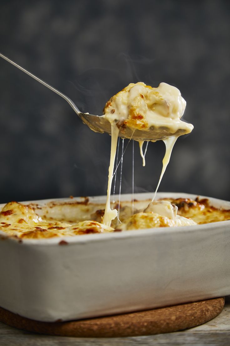 a spoon is lifting some food out of a casserole dish with cheese on top