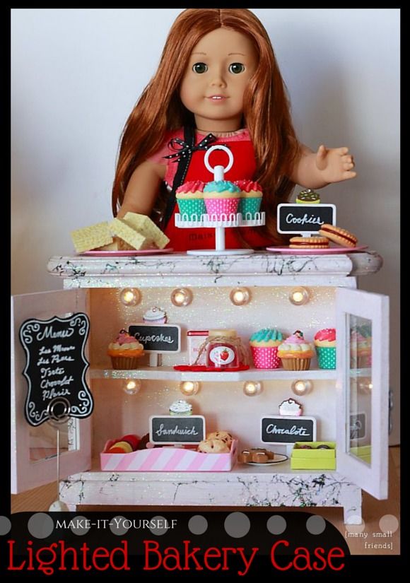 a doll is sitting on top of a display case with cakes and cupcakes