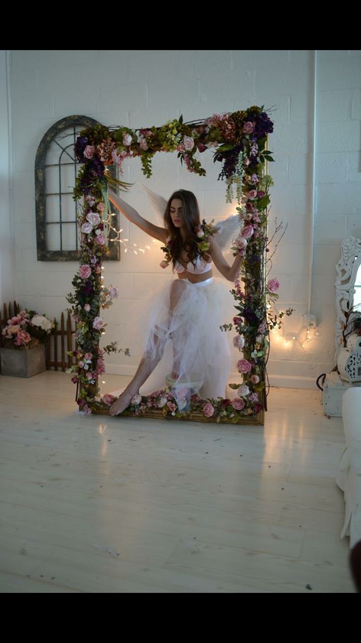 a woman standing in front of a mirror with flowers around her body and arms outstretched