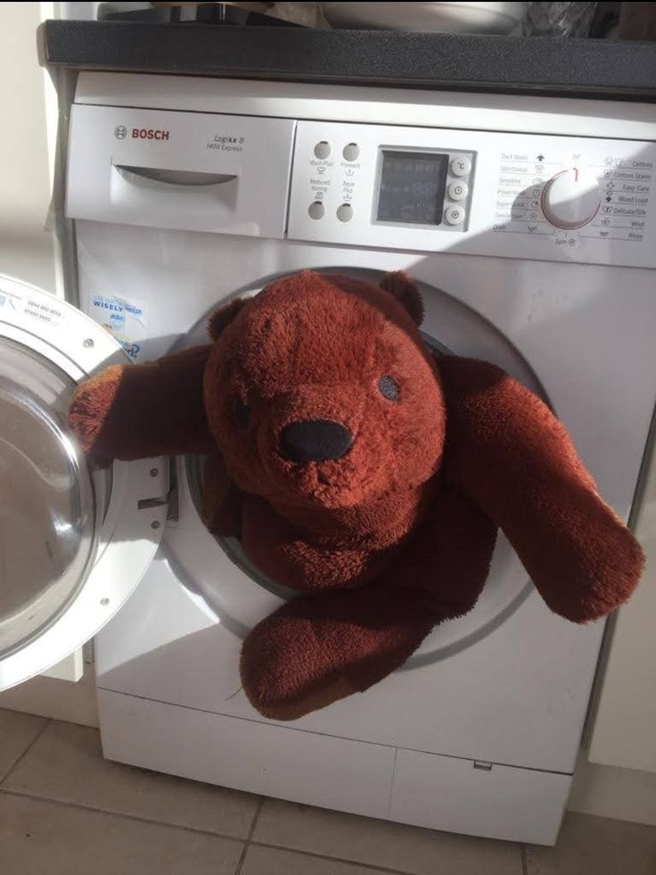 a teddy bear sitting on top of a dryer next to a white washer