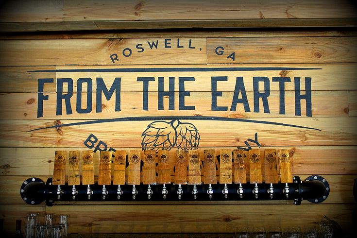 a wooden sign that says from the earth with wine glasses hanging on it's side