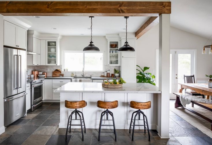 a kitchen with three stools in front of an island and two lights hanging from the ceiling