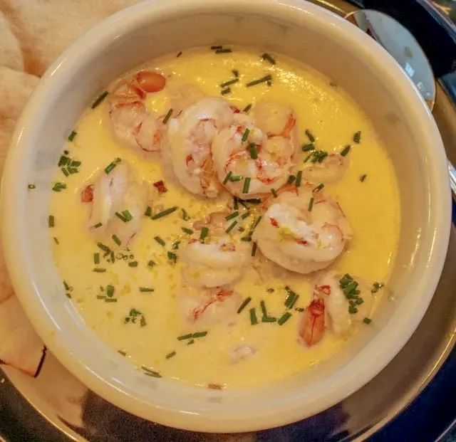 a white bowl filled with shrimp and grits on top of a plate next to chips