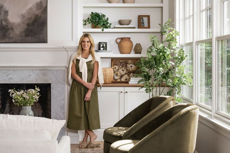 a woman standing next to a fireplace in a living room filled with furniture and decor