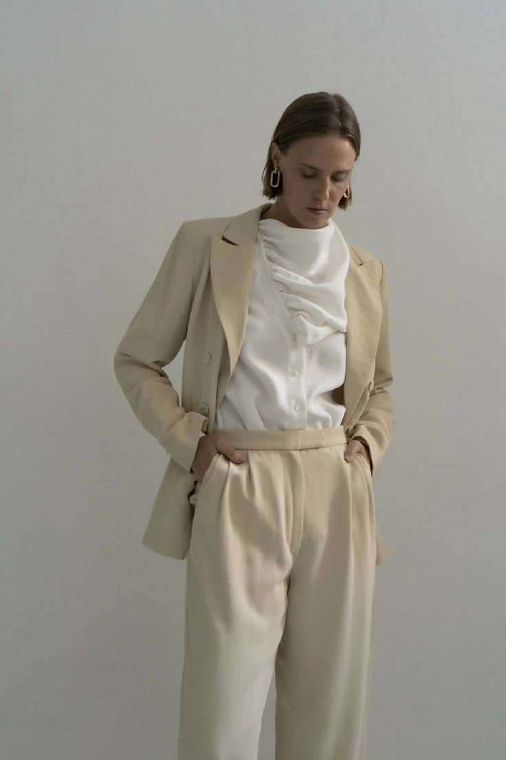 Slightly oversized and precisely tailored, the Rivne Beige Gentle Woman blazer is an emblem of modern luxury. Presented in a soft wool fabric, it features a double button fastening, open back detail with buttons two positions closure for a confident workwear choice. A modern classic, the matching Rivne tailored pants are cut with a loose fit and front belt pleats finished with split hems to elongate the leg and frame the ankle.Composition 100% pure woolTrimming: 100% metalButtons: 100% shellsDry Gentle Woman, Woman Blazer, Tailored Pants, Wool Suit, Women Artisans, Soft Wool, Sustainable Clothing, Wool Fabric, Split Hem