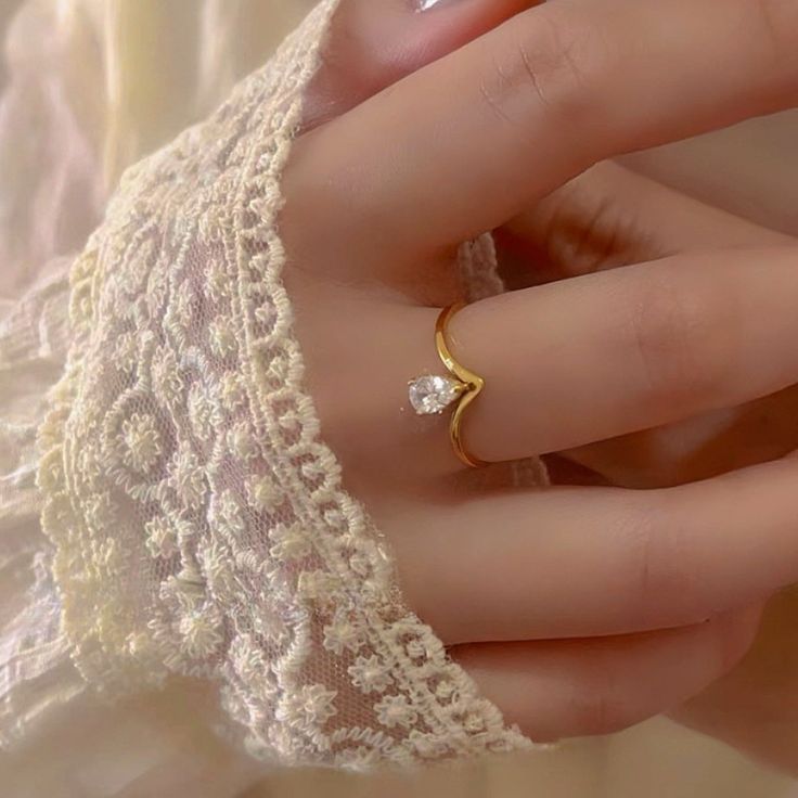 a woman's hand wearing a gold ring with a diamond on the middle finger