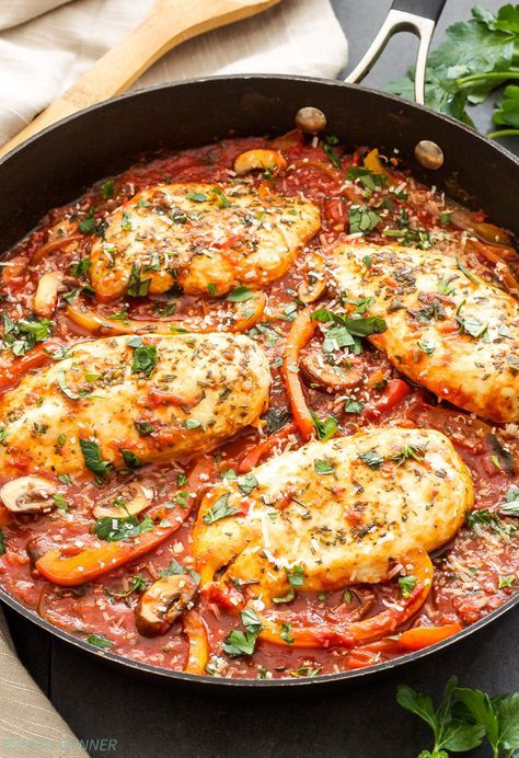 chicken with tomato sauce and parsley in a skillet on top of a table