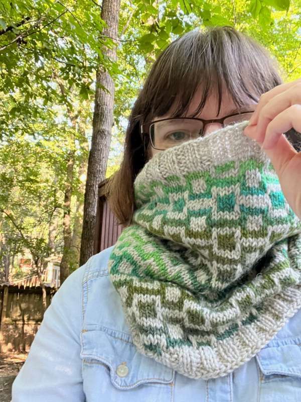 a woman wearing a green and white knitted cowl in front of some trees