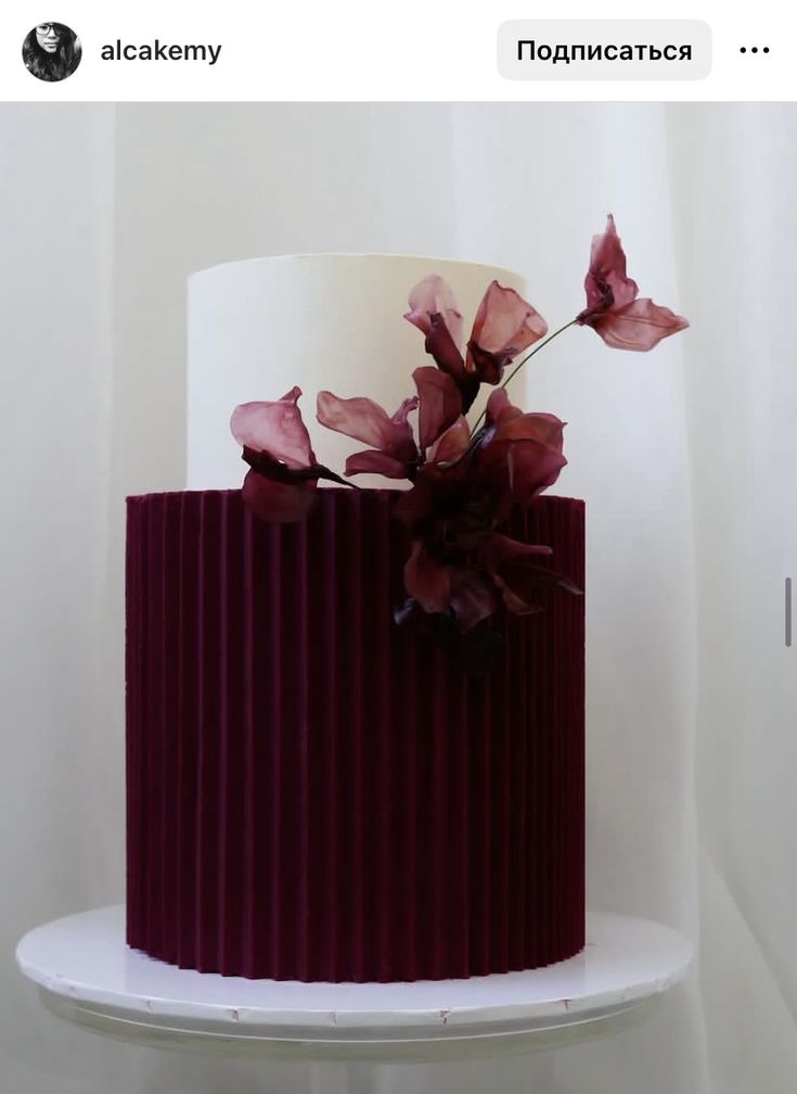 a red and white striped cake with flowers on the top is sitting on a shelf