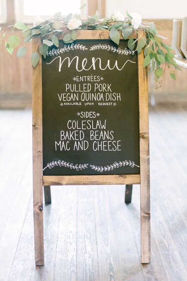 a chalkboard sign with greenery on it is sitting in the middle of a room