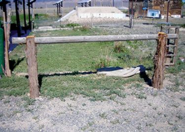 an old wooden fence in the middle of a field with grass and dirt on it