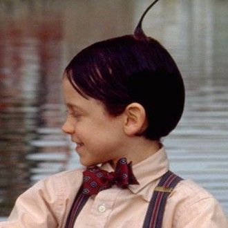 a young boy wearing suspenders and a bow tie holding something in his right hand