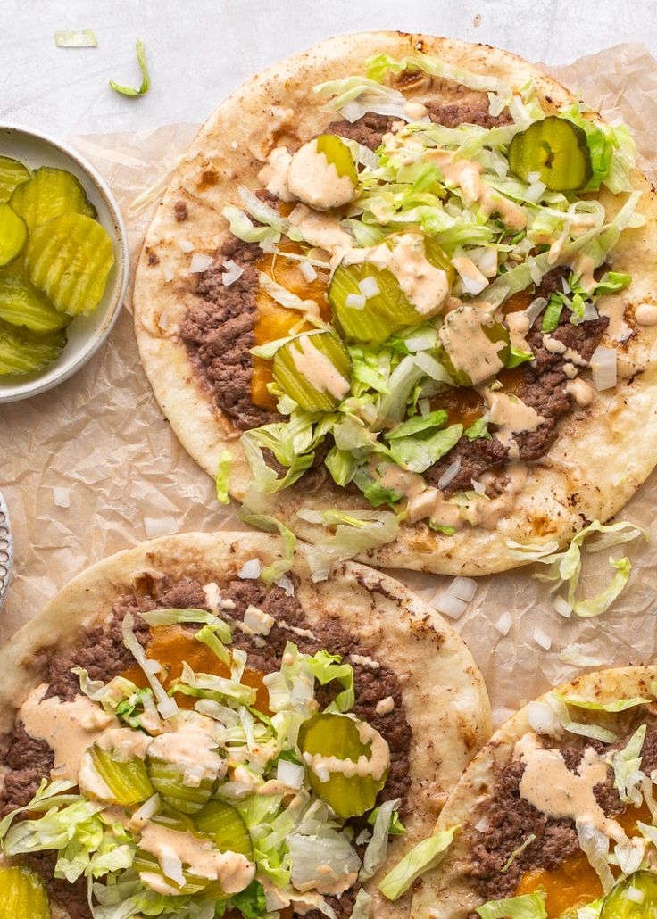 three pita breads with pickles and sauce on the top one is topped with lettuce