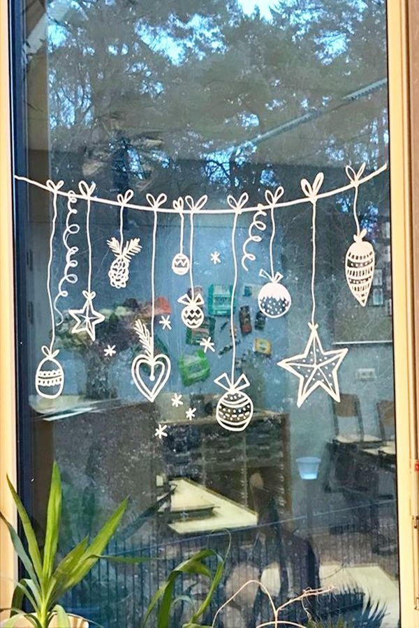 a window decorated with christmas ornaments hanging from it's side and surrounded by potted plants