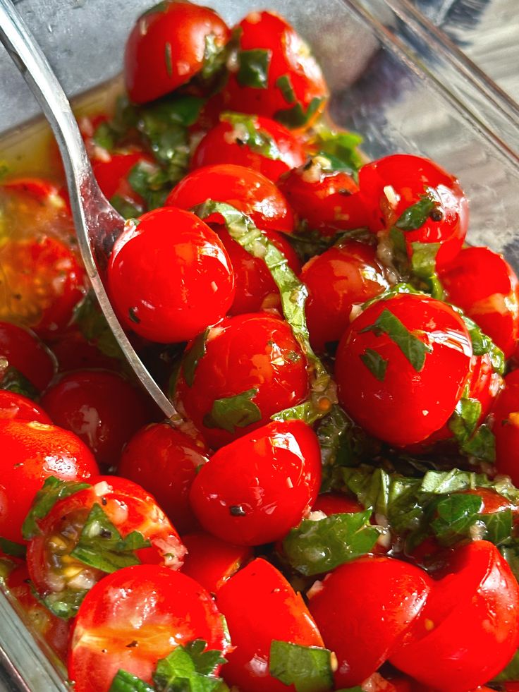 a glass bowl filled with lots of red tomatoes and green leaves on top of it