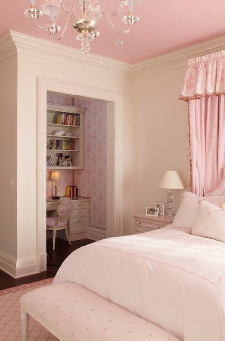 a white bed sitting under a pink chandelier next to a window in a bedroom