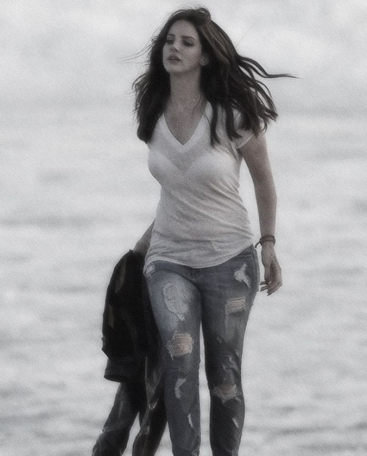 a woman is walking on the beach with an umbrella in her hand and wearing ripped jeans