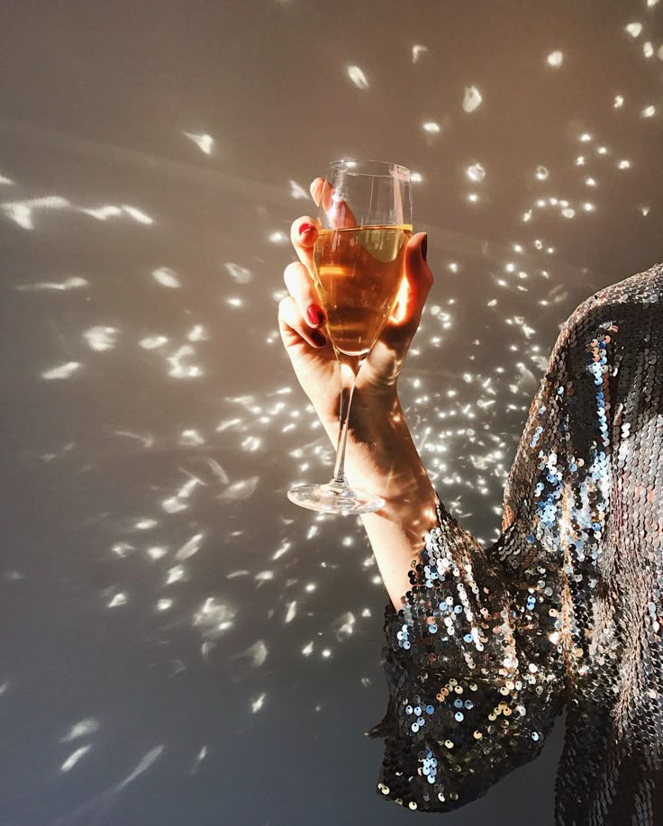 a woman holding a wine glass in front of a wall with light shining on it