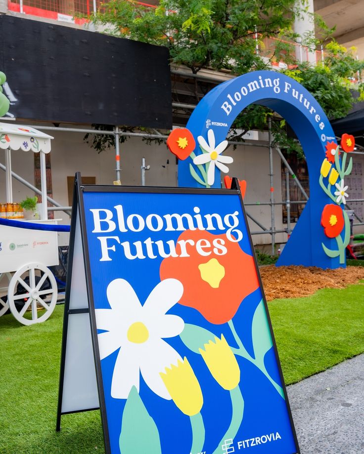 a sign that is sitting in the grass near some plants and flowers on display at blooming futures